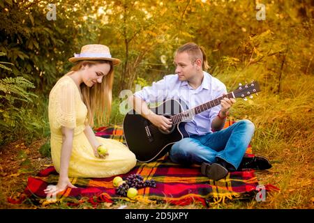 Bild eines jungen Mannes, der Gitarre für ein Mädchen spielt Im Park Stockfoto