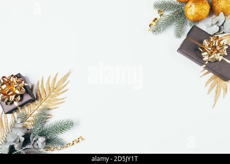 Weihnachtliche flache Lay-Anordnung mit Geschenkschachteln, goldenen Bändern, Glitzerkugeln-Ornamenten und Tannenzweigen auf weißem Hintergrund. Stockfoto