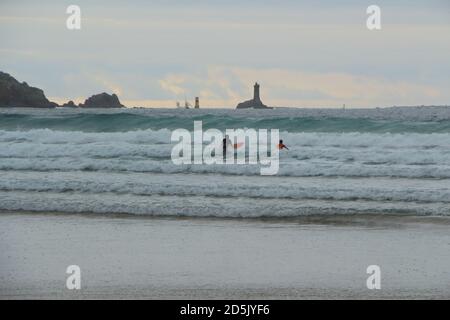 Zwei Surfer am Strand Baie des Trepasses in Plogoff mit Leuchtturm La Vieille im Hintergrund Stockfoto