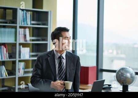 asiatische Corporate Executive denken im Büro mit einer Tasse Kaffee in der Hand Stockfoto