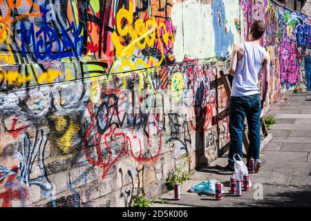 Ein junger Mann bereitet sich darauf vor, Graffiti an eine Wand zu sprühen. Stockfoto