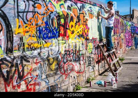 Ein junger Mann, der Graffiti an eine Wand sprüht. Stockfoto