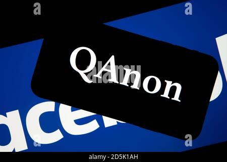 QAnon im Vergleich ZU FACEBOOK. QAnon-Unternehmenslogo auf dem Smartphone, das auf Facebook-Logos platziert ist. Konzept für das Verbot von QAnon in sozialen Medien. Stockfoto