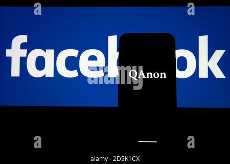 QAnon im Vergleich ZU FACEBOOK. QAnon-Unternehmenslogo auf dem Smartphone, das auf Facebook-Logos platziert ist. Konzept für das Verbot von QAnon in sozialen Medien. Stockfoto