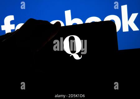 QAnon im Vergleich ZU FACEBOOK. QAnon-Unternehmenslogo auf dem Smartphone, das auf Facebook-Logos platziert ist. Konzept für das Verbot von QAnon in sozialen Medien. Stockfoto