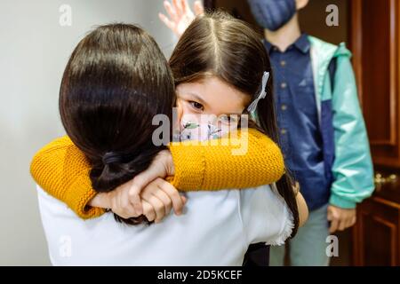 Mutter umarmt Tochter mit Maske kommen zurück von der Schule Stockfoto