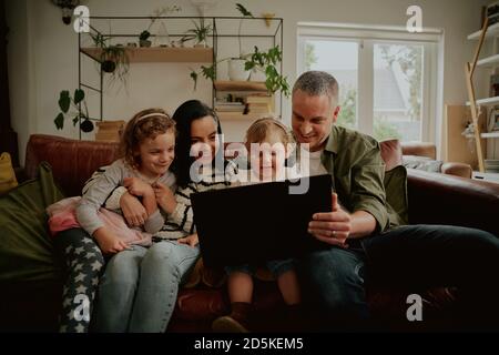 Portrait von Kleinkind mit Vater Hilfe halten Laptop während der Beobachtung Lustige Videos online, während Sie sich zu Hause bei covid-19 Lockdown entspannen Stockfoto