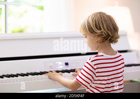 Kind spielt Klavier. Kinder spielen Musik. Klassische Erziehung für Kinder. Kunstunterricht. Kleiner Junge an der weißen digitalen Tastatur. Instrument für junge Studenten Stockfoto