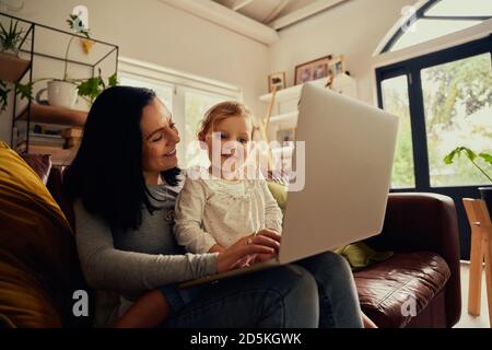 Mädchen und Frau sitzen zusammen auf der Couch zu Hause beobachten Lustige Cartoon-Video auf Laptop während covid-19 Lockdown Stockfoto