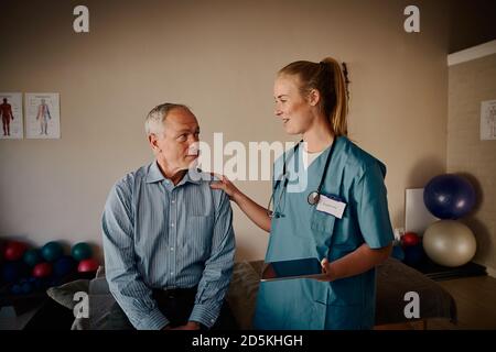 Lächelnde Krankenschwester, die den älteren Patienten unterstützt, nachdem sie Berichte auf digitaler Basis gezeigt hat Tablet im Krankenhaus Stockfoto