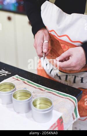 Ein Chandler oder Kerzenmacher fügt einen Docht zu duftenden Handgemachte Kerzen Stockfoto