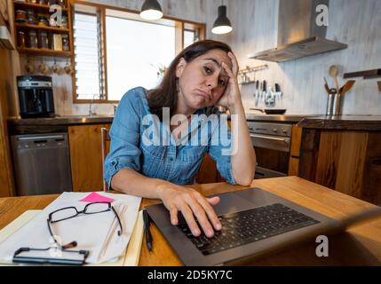 Gestresste Geschäftsfrau, die von zu Hause aus auf einem Laptop arbeitet und besorgt, müde und überfordert aussieht. Erschöpfte Frau, die während der sozialen Distanz fernarbeitet Stockfoto
