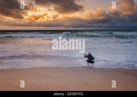 Ein Urlauber, der mit seinem Handy einen spektakulären Sonnenuntergang über Fistral Beach in Newquay in Cornwall fotografiert. Stockfoto