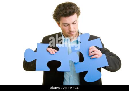 Junger Mann im Anzug mit zwei Puzzleteilen in der Hand Stockfoto