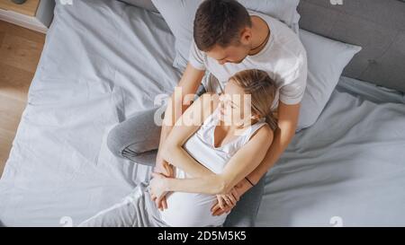 Happy Young couple Kuscheln zusammen im Bett, junge Frau ist schwanger und liebevollen Ehemann hält sie in Umarmung und streichelt ihren Bauch zärtlich Stockfoto