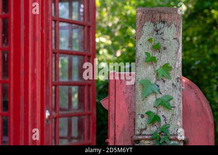 Verwitterter englischer Briefkasten auf Efeu bedeckten Pfosten in einem kleinen Dorf im ländlichen England. Traditionelle englische Telefonbox im Hintergrund. Post-Mail eng Stockfoto