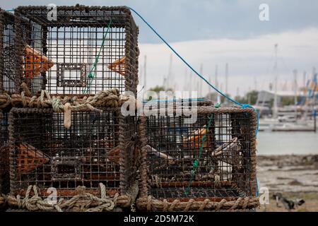 Hummer Töpfe an der Küste zusammengebunden bereit für den Einsatz an einem grauen Tag. Yachten und Yachthafen im Hintergrund. Fischerei Küste Ebbe. Stockfoto