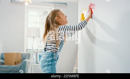 Happy Little Girl taucht ihre Hände in Gelb und Rot und beginnt mit dem Malen an der Wand. Sie hat Spaß und lacht. Das Haus wird renoviert. Stockfoto