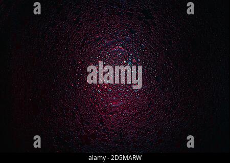 Rote, blaue und violette Öltröpfchen mit farbigen Glühbirne mit dunklem Hintergrund beleuchtet. Wasser und Olivenöl Mischung. Stockfoto