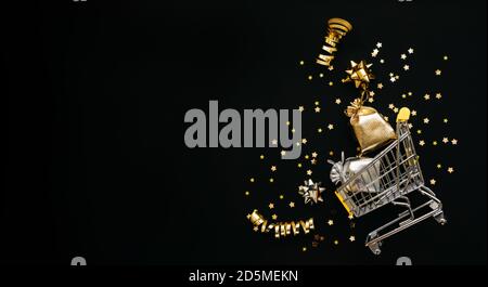 Warenkorb und verschiedene Goldartikel auf schwarzem Hintergrund. Festliches konzeptionelles Weihnachtsbanner oder Neujahrsbanner mit Leerzeichen für Text. Stockfoto