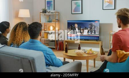 Glückliche Freunde Sitzen Zu Hause Und Schauen Sich Nachrichten An. Entspannen auf einer Couch.Right gemütliche Wohnung mit Freunden essen Snacks und Spaß haben. Stockfoto