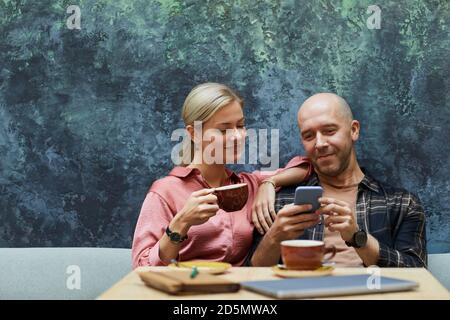 Junges Paar sitzt im Café zusammen mit Handy und Kaffee trinken Stockfoto