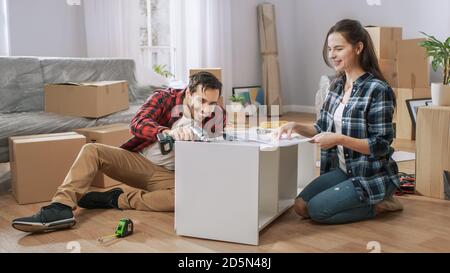 Happy couple Montage von Möbeln als Team, Mädchen liest Anweisungen und Junge zieht Schraube mit einem Bohrer. Umzug in neue Wohnung, paar montieren Stockfoto