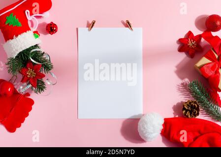 Weihnachtskarte mit imitiertem Blankopapier und Weihnachtsrahmen aus Weihnachtsaccessoires und Geschenkschachteln auf hellrosa Hintergrund, Kopierfläche. Flach liegend. Stockfoto