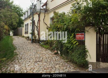 Malerische gepflasterte Straße in Střešovičky, auch bekannt als Malé Střešovice (kleine Střešovice) in Prag, Tschechische Republik. Střešovičky ist eine ehemalige Arbeitersiedlung mit kleinen Häusern aus dem Ende des 18. Jahrhunderts, die ihre ursprüngliche Atmosphäre im Laufe der Jahrhunderte unberührt erhalten hat und heute als romantischer Ort ohne Touristen in den Prager Außenbezirken bekannt ist. Die Ecke Na Kocourkách Gasse und Pod Adnělkou Straße ist auf dem Foto dargestellt. Stockfoto