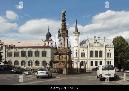 Die Säule der Heiligen Dreifaltigkeit (Sloup Nejsvětější Trojice) wurde vom böhmischen Bildhauer Ondřej Dudke (1708) auf dem Hauptplatz in Zákupy in Nordböhmen, Tschechische Republik, entworfen. Im Hintergrund ist das neugotische Gebäude des Rathauses (1867) zu sehen. Stockfoto