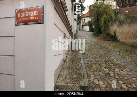 Malerische gepflasterte Straße in Střešovičky, auch bekannt als Malé Střešovice (kleine Střešovice) in Prag, Tschechische Republik. Střešovičky ist eine ehemalige Arbeitersiedlung mit kleinen Häusern aus dem Ende des 18. Jahrhunderts, die ihre ursprüngliche Atmosphäre im Laufe der Jahrhunderte unberührt erhalten hat und heute als romantischer Ort ohne Touristen in den Prager Außenbezirken bekannt ist. Auf dem Foto ist die Ecke Ve Střešovičkách Street und K Bateriím Lane zu sehen. Stockfoto