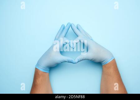Zwei männliche Hände in blauem Latex sterile medizinische Handschuhe zeigen eine Geste des Herzens auf blauem Hintergrund, Konzept von Güte, Hilfe und Freiwilligenarbeit Stockfoto