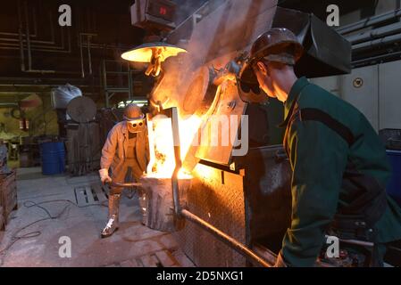 Arbeitnehmer in einer Gießerei gießen ein Werkstück aus Metall - Sicherheit bei der Arbeit und Teamarbeit Stockfoto