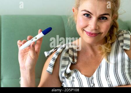Glückliche blonde Frau hält einen Schwangerschaftstest. Stockfoto