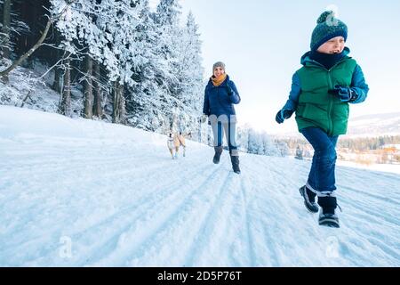 Mutter und Sohn haben einen Spaß. Sie laufen mit ihrem Beagle-Hund im verschneiten Wald während des Hundespaziergangs. Mutter und Sohn Verwandte und Weiblichkeit Werte Konzept im Stockfoto