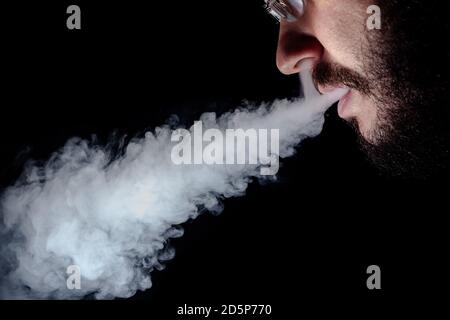 Ein Mann mit einem schwarzen Bart und einem Schnurrbart Brille raucht eine Shisha und atmet einen Rauchstrom aus Stockfoto