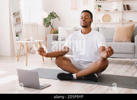 Schwarzer Mann Meditierend Tun Yoga Sitzen Am Laptop Zu Hause Stockfoto