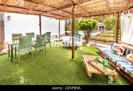 Außenpanorama eines Hinterhofs mit einem Loungebereich in einer entspannenden Ferienvilla mit Sofas, Kissen, Tisch, Stühlen, Gras, Garten und Pool Stockfoto