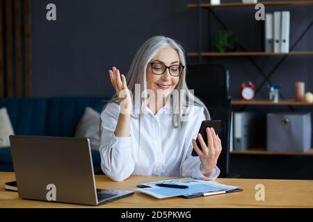Ältere grauhaarige schöne Frau mit Smartphone und lächeln. Glückliche Geschäftsfrau mit Handy-Apps, SMS-Nachrichten, Surfen im Internet Stockfoto