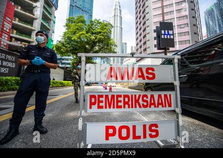 Kuala Lumpur, Malaysia. Oktober 2020. Ein Polizist und ein Soldat überprüfen Fahrzeuge an einer Straßensperre in Kuala Lumpur, Malaysia, 14. Oktober 2020. Malaysia kündigte am Montag die Wiedereinführung von Maßnahmen zur Einschränkung der Freizügigkeit in mehreren Bereichen an, um die jüngste Spitze der COVID-19-Fälle einzudämmen. Die Maßnahmen werden vom 14. Bis 27. Oktober in Kuala Lumpur, dem Verwaltungszentrum von Putrajaya sowie dem angrenzenden Staat Selangor in Kraft treten, als Reaktion auf die tägliche Erhöhung der neuen COVID-19-Fälle, mit den Maßnahmen, die die Kette von Infektionen zu durchbrechen. Quelle: Zhu Wei/Xinhua/Alamy Live News Stockfoto