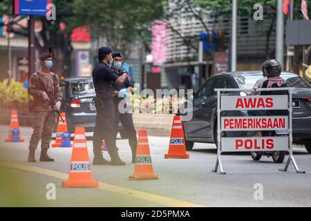 Kuala Lumpur, Malaysia. Oktober 2020. Polizisten und ein Soldat überprüfen Fahrzeuge an einer Straßensperre in Kuala Lumpur, Malaysia, 14. Oktober 2020. Malaysia kündigte am Montag die Wiedereinführung von Maßnahmen zur Einschränkung der Freizügigkeit in mehreren Bereichen an, um die jüngste Spitze der COVID-19-Fälle einzudämmen. Die Maßnahmen werden vom 14. Bis 27. Oktober in Kuala Lumpur, dem Verwaltungszentrum von Putrajaya sowie dem angrenzenden Staat Selangor in Kraft treten, als Reaktion auf die tägliche Erhöhung der neuen COVID-19-Fälle, mit den Maßnahmen, die die Kette von Infektionen zu durchbrechen. Quelle: Zhu Wei/Xinhua/Alamy Live News Stockfoto