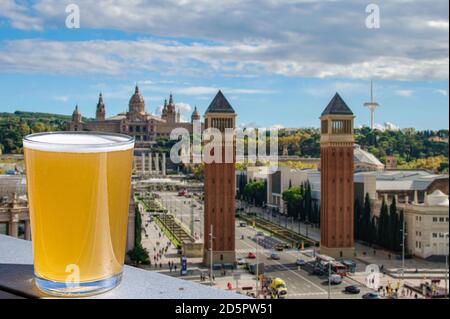 Ein Glas helles Bier mit Blick auf den Plaza de la Espanya in Barcelona, Spanien. Luftaufnahme der Placa d'Espanya mit venezianischen Türmen. Stockfoto