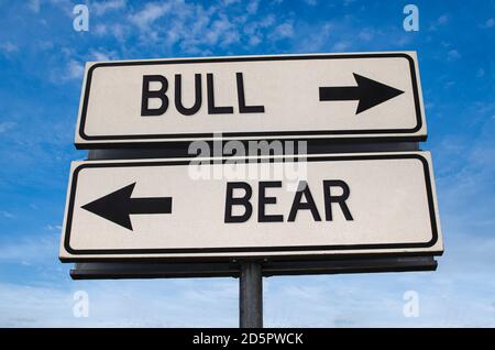 Stier gegen Bär. Weiße zwei Straßenschilder mit Pfeil auf Metallmast mit Wort. Richtungsstraße. Kreuzung Straßenschild, Zwei Pfeil. Blauer Himmel Hintergrund. Zwei w Stockfoto