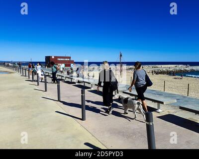 Menschen, die entlang der Promenade in der Nähe des Strandes gehen. Passeig maritim del Port Olimpic, Platja de la Nova Icària. Barcelona, Katalonien, Spanien. Stockfoto