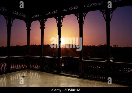 Blick auf den Sonnenuntergang auf dem See im Frühjahr aus Holz durchbrochene Galerie oder Pavillon. Wald und See in den Strahlen der Sonne. Stockfoto