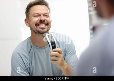 Lächelnder Mann steht vor einem Spiegel und hält Rasiermesser in den Händen. Stockfoto