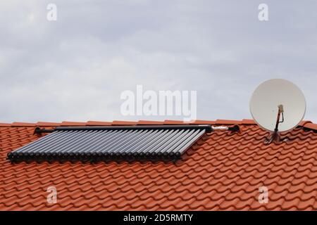 Vakuum-Kollektoren - Solar-Wasser-Heizung auf dem roten Dach des Hauses mit Satellit. Stockfoto