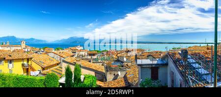 Panorama von Desenzano del Garda Stadt mit roten Ziegeldächern Gebäude, Gardasee Wasser, Monte Baldo Bergkette, Halbinsel Sirmione, Lombardei, Norditalien. Luftpanorama von Desenzano Stockfoto