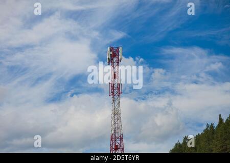 Ein Zellturm aus rot-weißem Metall in einem unzugänglichen Platz in den Altai-Bergen vor dem Hintergrund von Grün Nadelbäume für die Übertragung Stockfoto