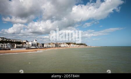 Hastings, East Sussex, England. Die Strandpromenade zum Küstenort an der britischen Südküste mit seinem Wahrzeichen Burg sichtbar auf dem Hügel. Stockfoto